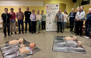 Gruppenfoto des HERZSICHER-Kurses in Goldbeck mit Teilnehmenden, Übungspuppen und AED-Trainingsgerät.