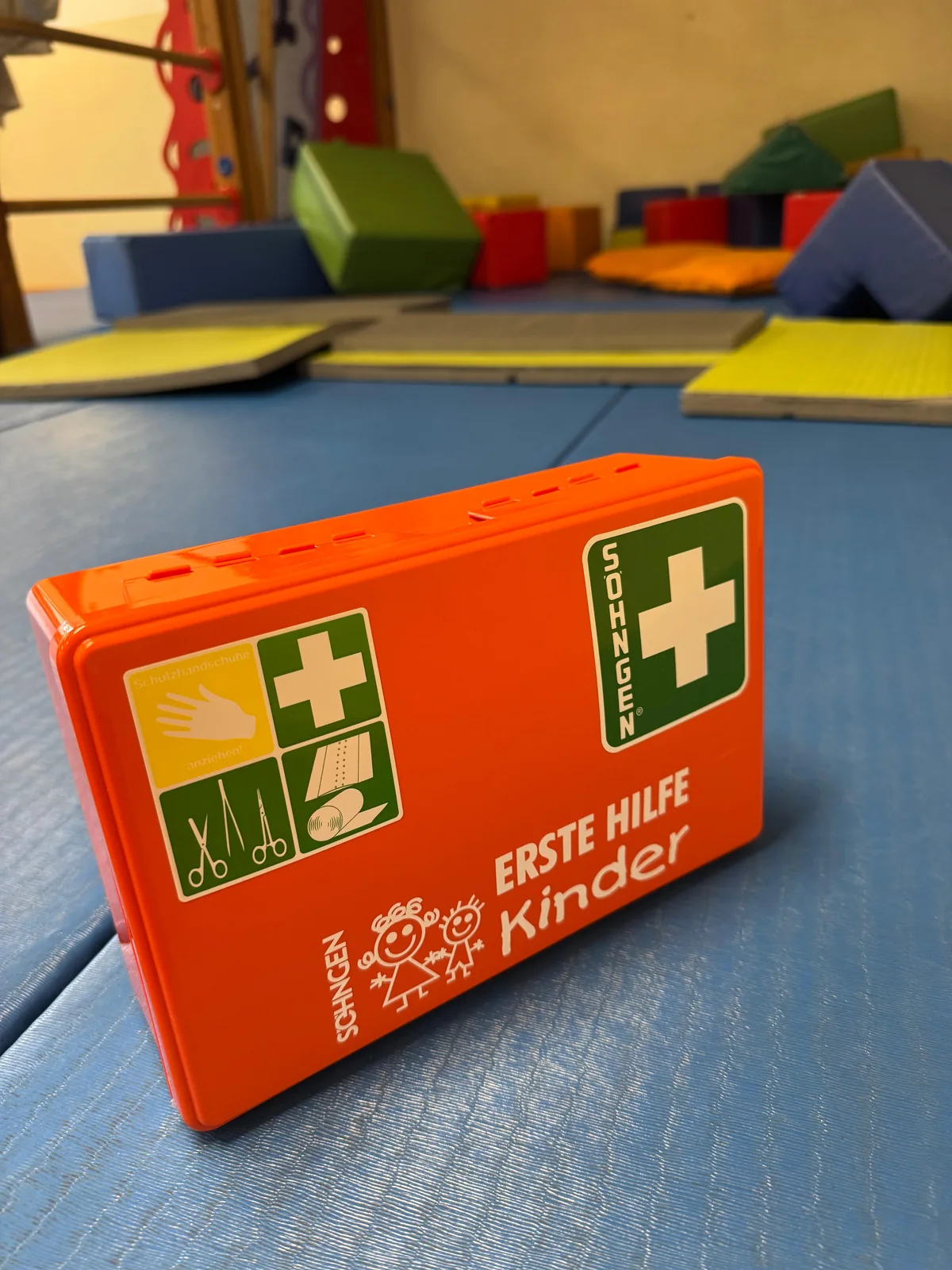 Erste-Hilfe-Koffer für Kinder auf Turnmatten in einem Bewegungsraum.