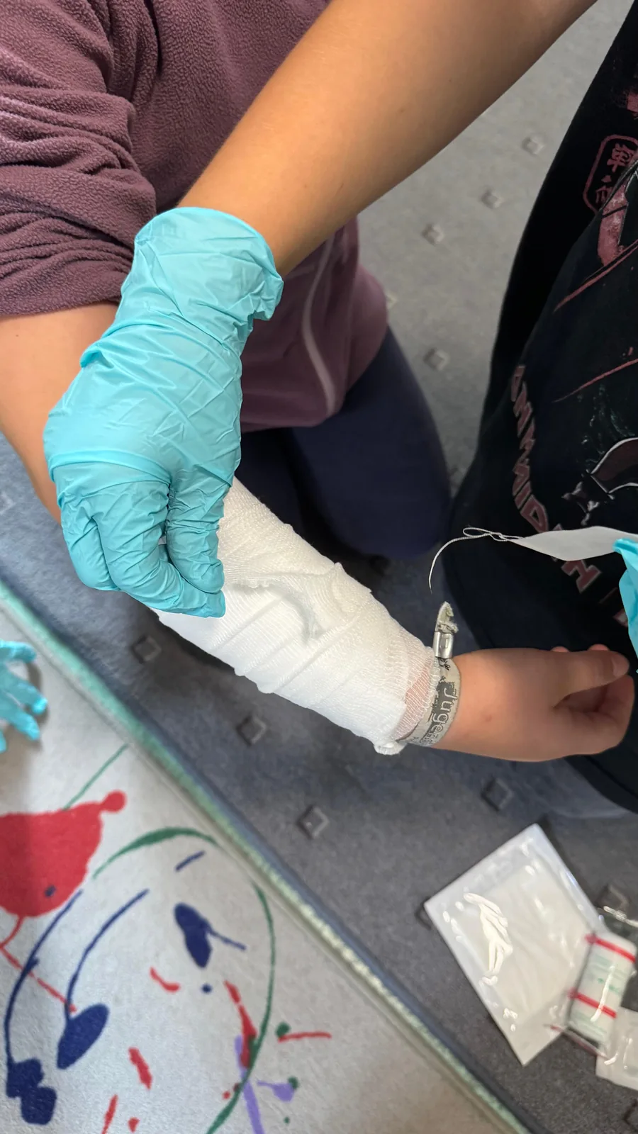 pulsretter-minihelden-verband Kinder üben mit Handschuhen das Anlegen eines Unterarmverbands.