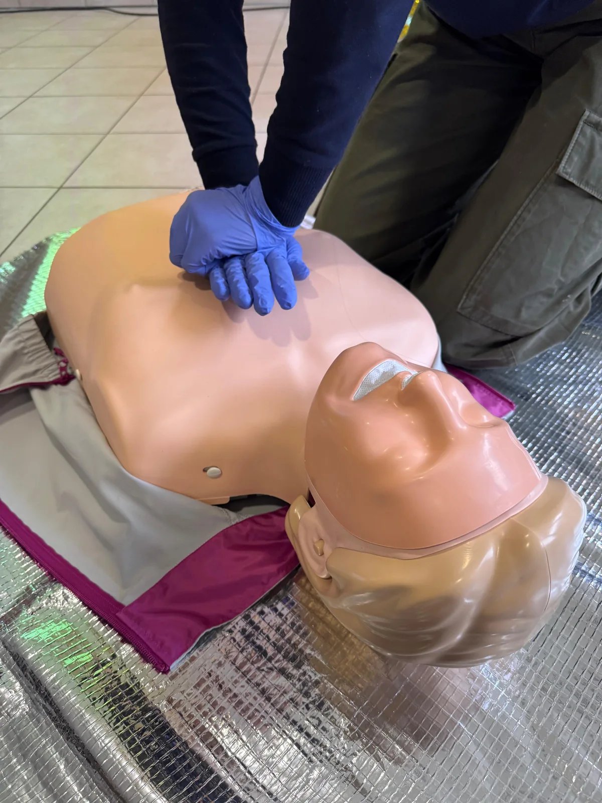Hände mit Einmalhandschuhen üben die Herzdruckmassage an einem Reanimationsmodell.