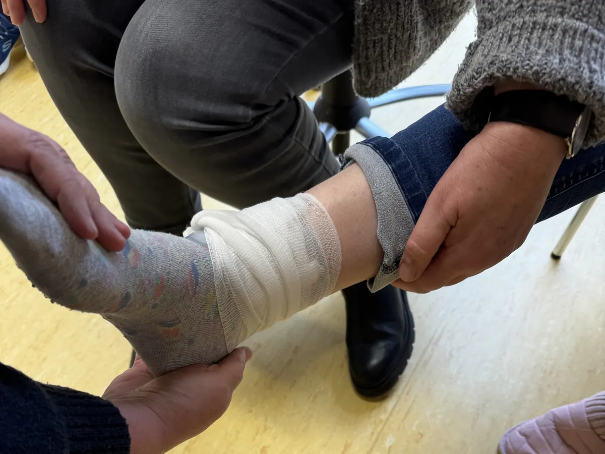 pulsretter-verband-sprunggelenk Hände legen in einer praktischen Übung einen Verband am Sprunggelenk an.